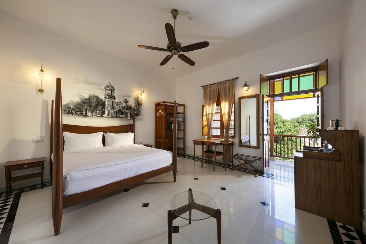 Une chambre à coucher avec un lit à baldaquin, un bureau, une chaise, une armoire et un balcon donnant sur un paysage verdoyant.