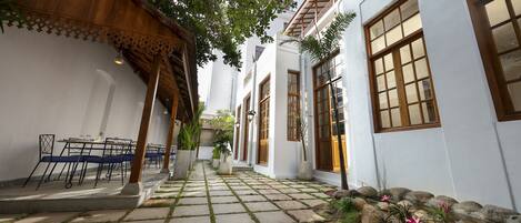Un patio con suelo de baldosas, mobiliario exterior, plantas en macetas y una pérgola de madera.