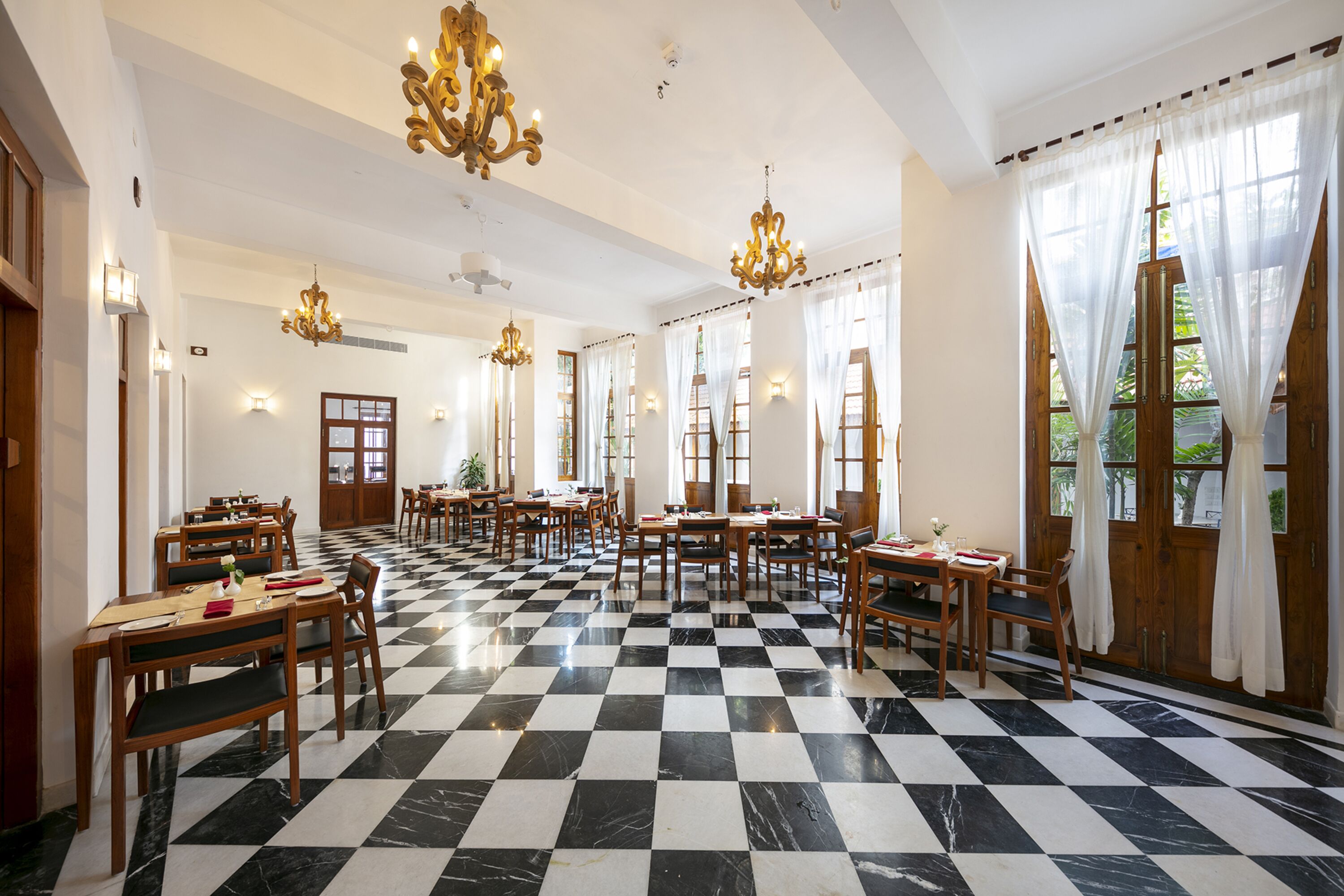 Une salle à manger d’hôtel avec un sol à carreaux, des tables et des chaises en bois.