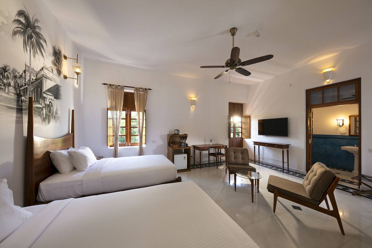 Une chambre d’hôtel comprenant un lit, un bureau, une chaise, un ventilateur de plafond, une télévision et une salle de bain avec un lavabo et un miroir.