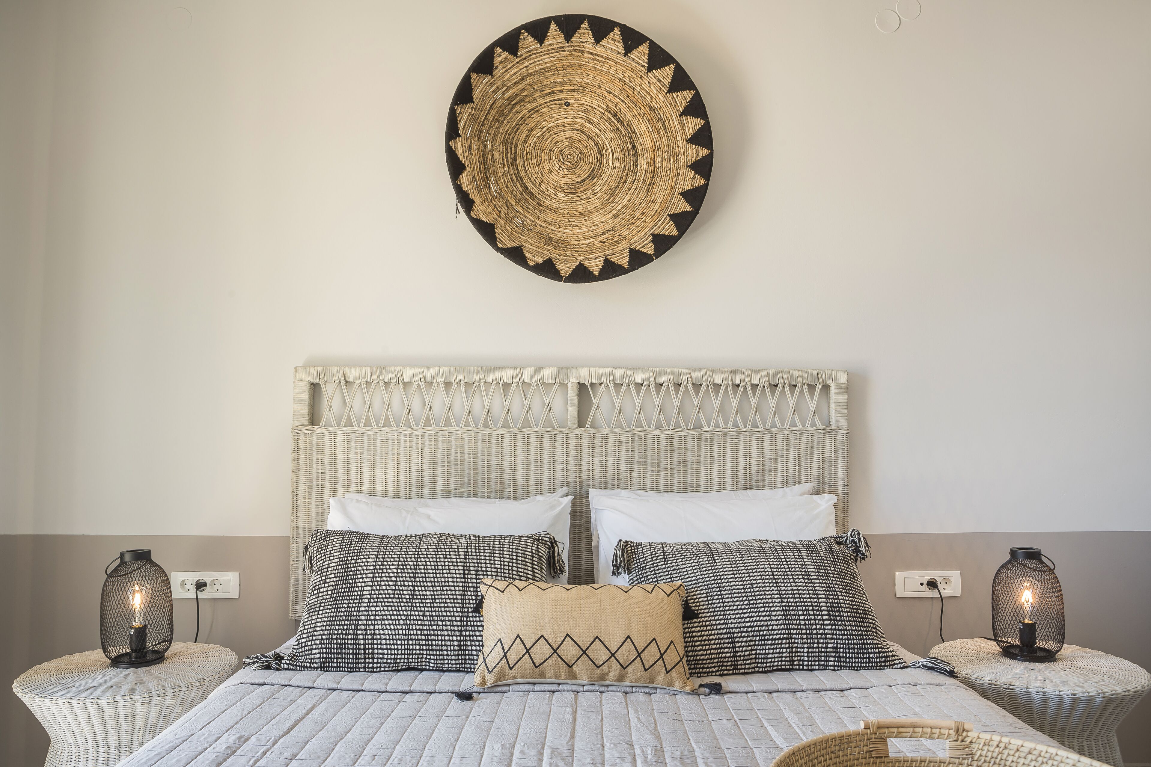 A bed with a woven headboard, two bedside tables with lamps, and a wall-mounted circular decoration.