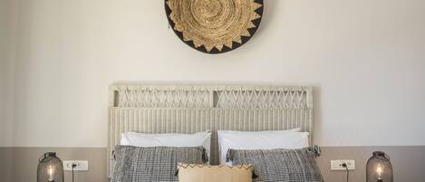 A bed with a woven headboard, two bedside tables with lamps, and a wall-mounted circular decoration.