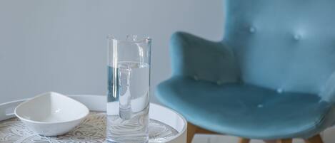 A white table with a glass of water, a white bowl, and a teal chair.