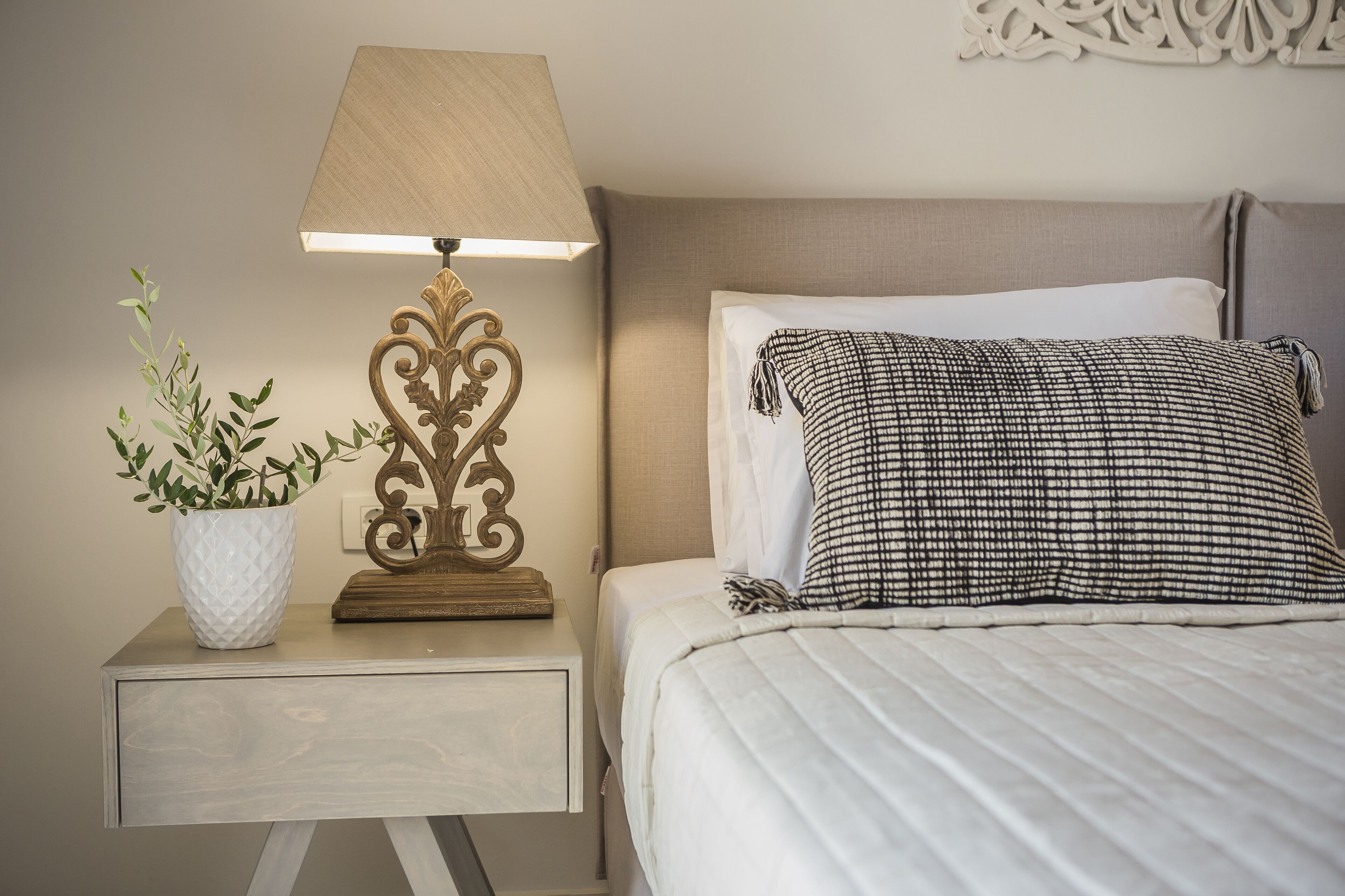 A neatly made bed with a checkered pillow, a bedside lamp, and a potted plant on a bedside table.