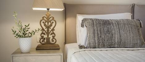 A neatly made bed with a checkered pillow, a bedside lamp, and a potted plant on a bedside table.