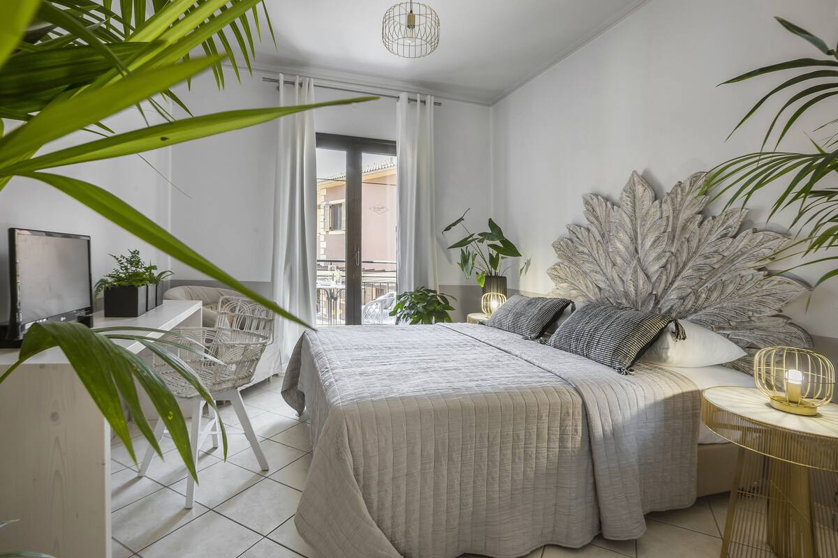 A modern bedroom with a bed, bedside tables, a desk, and a large plant.