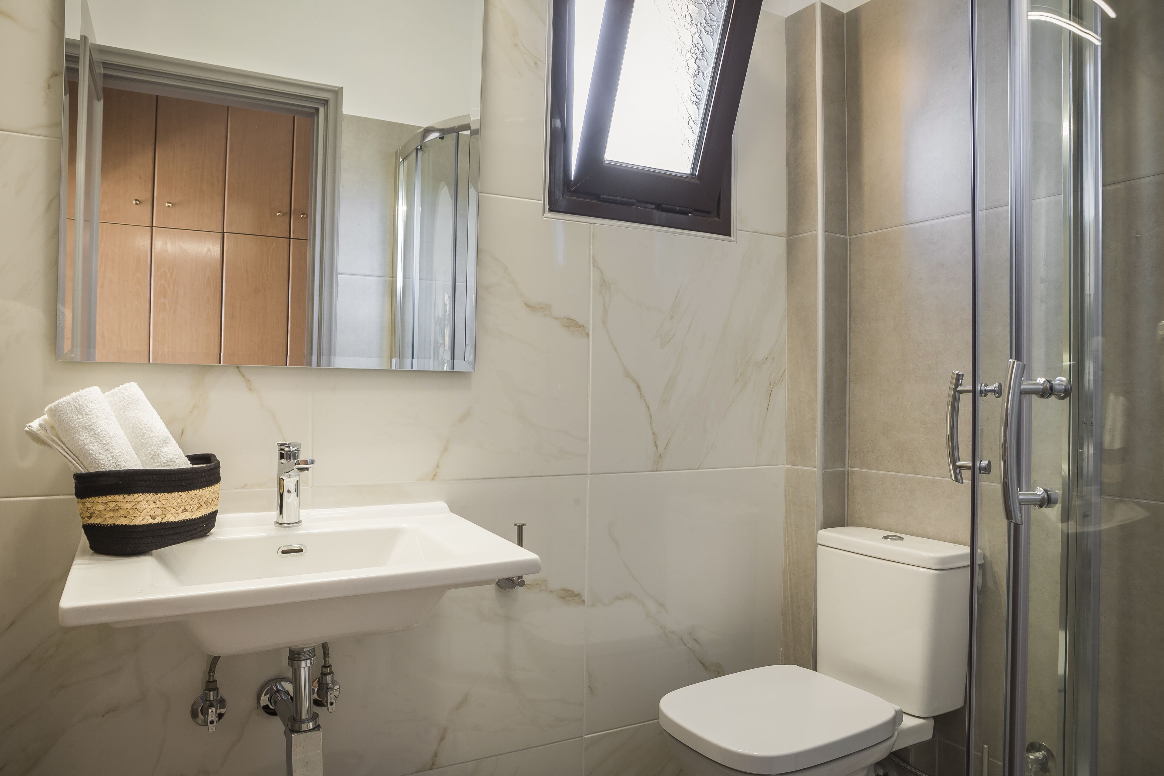 Un baño con lavabo, espejo, toallero, inodoro y cabina de ducha de vidrio.