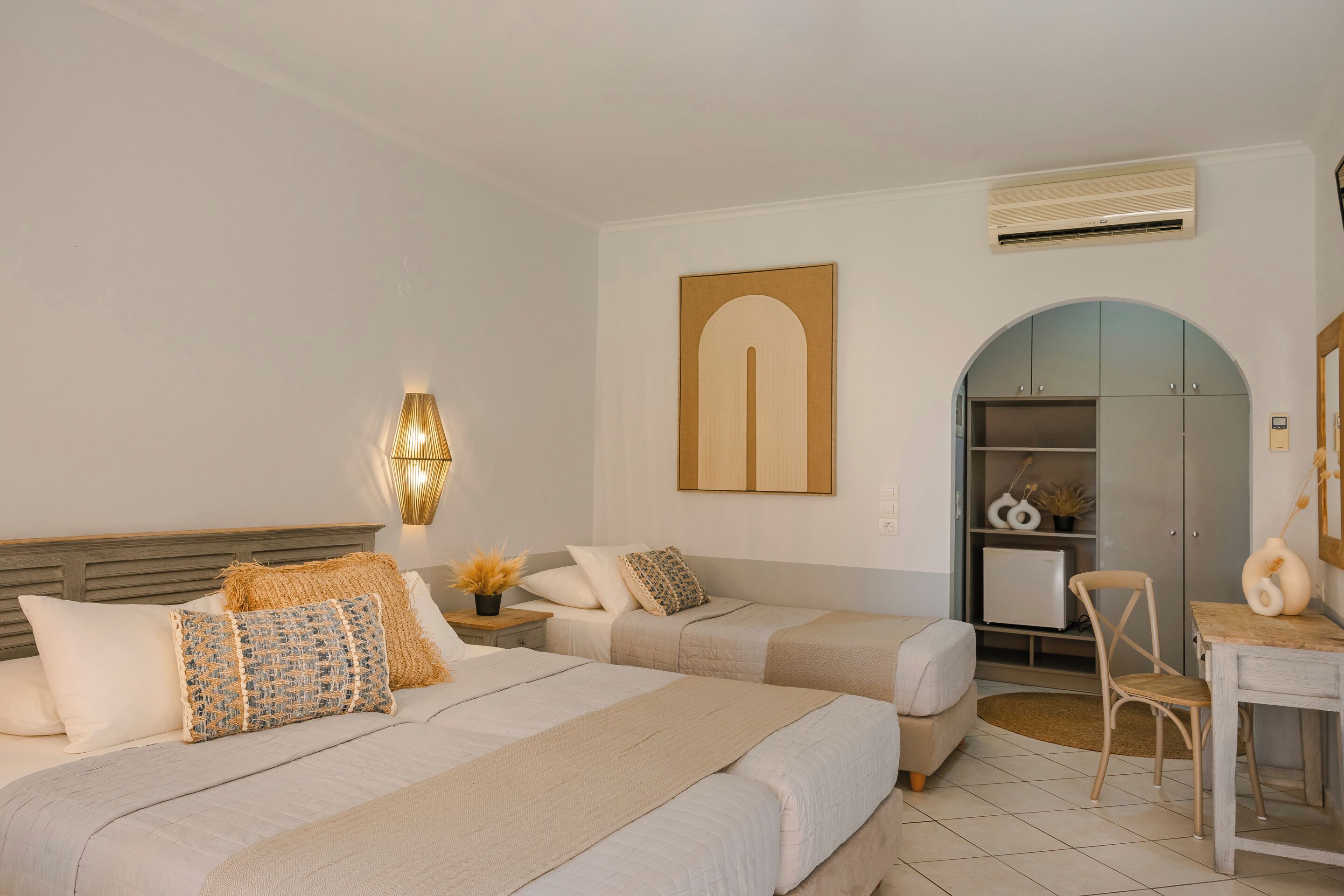 A hotel room with two beds, a desk, a chair, a wardrobe, and a wall-mounted air conditioner.