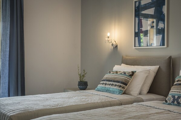 A bedroom with a bed, pillows, a nightstand, a wall-mounted light, and a framed abstract painting. - Makis Hotel Skala (Kefalonia)