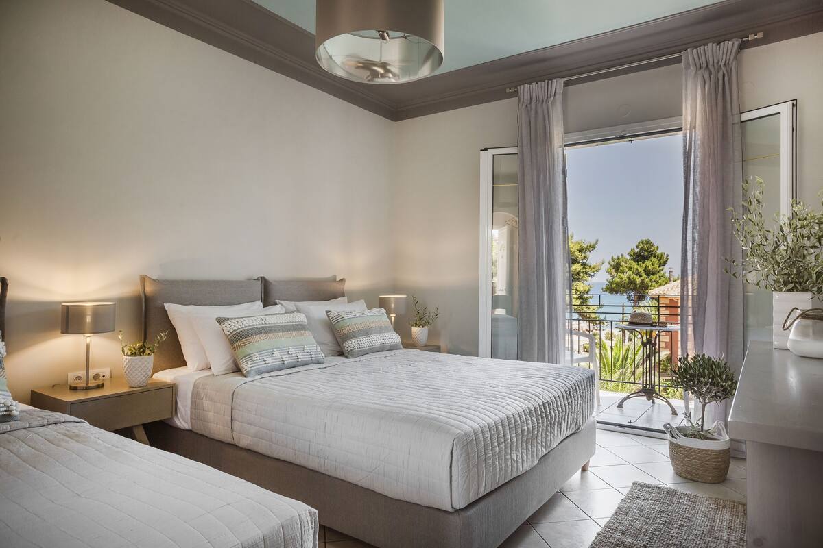 A modern bedroom with a large bed, bedside tables, a lamp, and a view of the outside balcony.