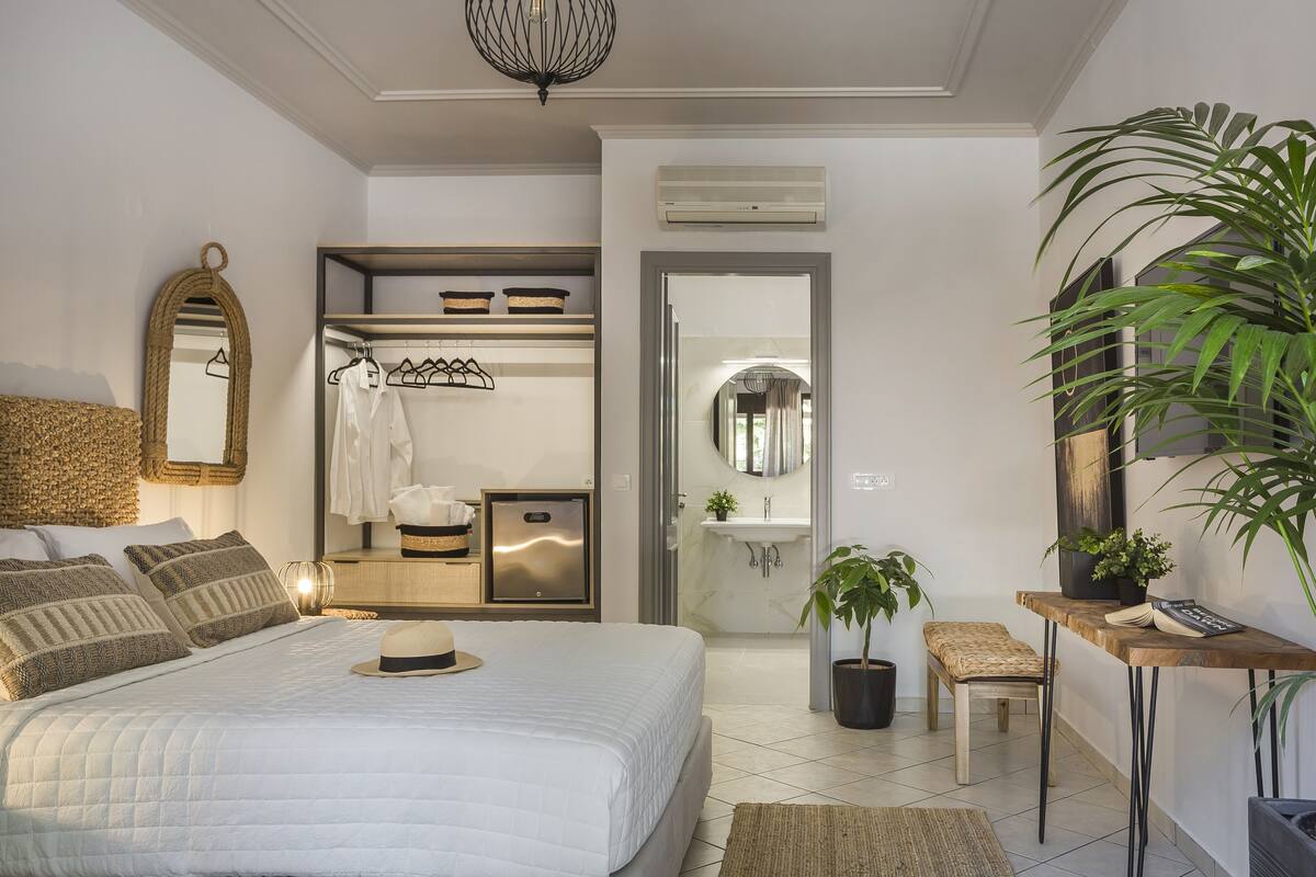A modern bedroom with a large bed, a wardrobe, a vanity with a mirror, a small table, and a potted plant.