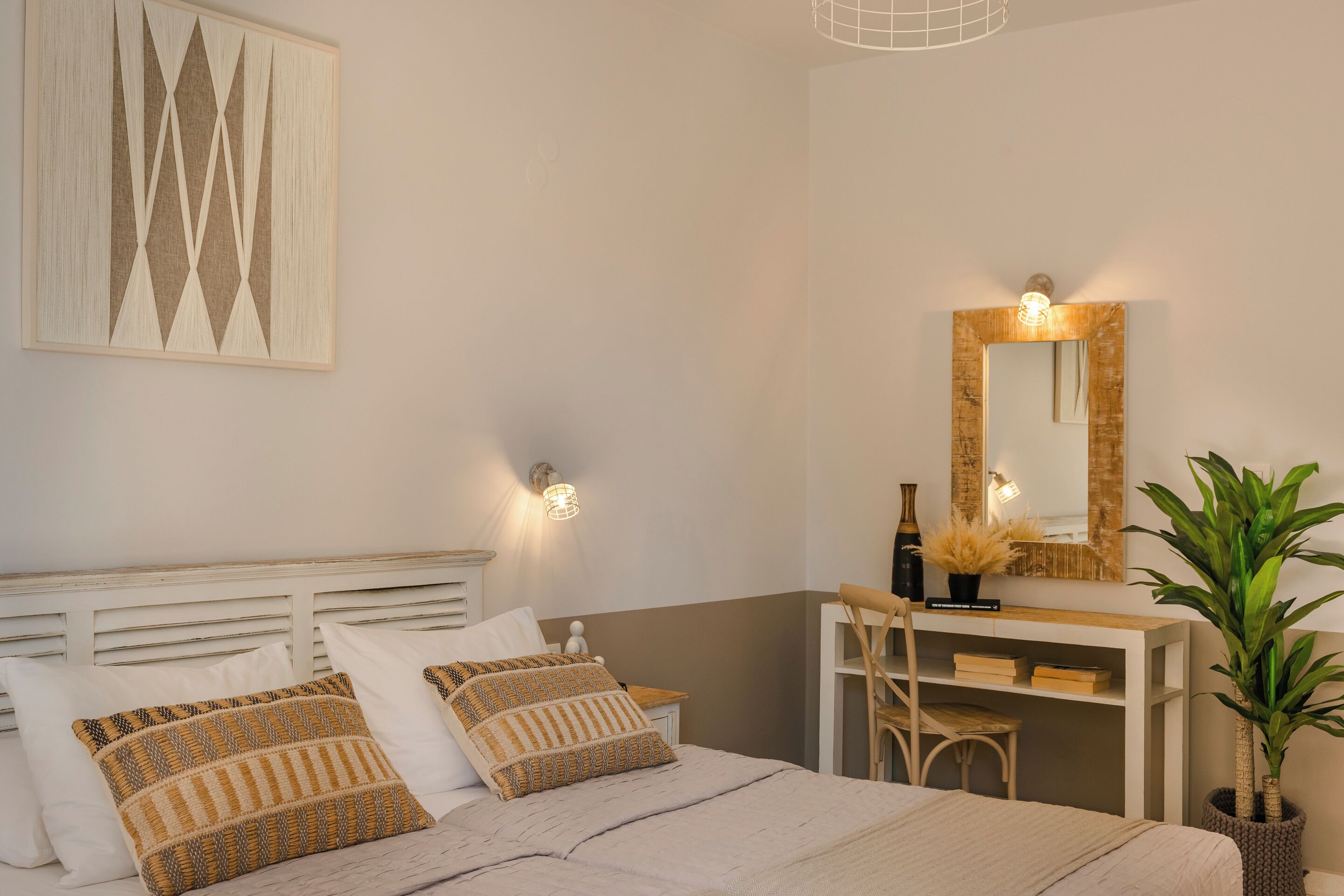 A bedroom with a bed, bedside tables, a desk, a chair, a mirror, and a potted plant.
