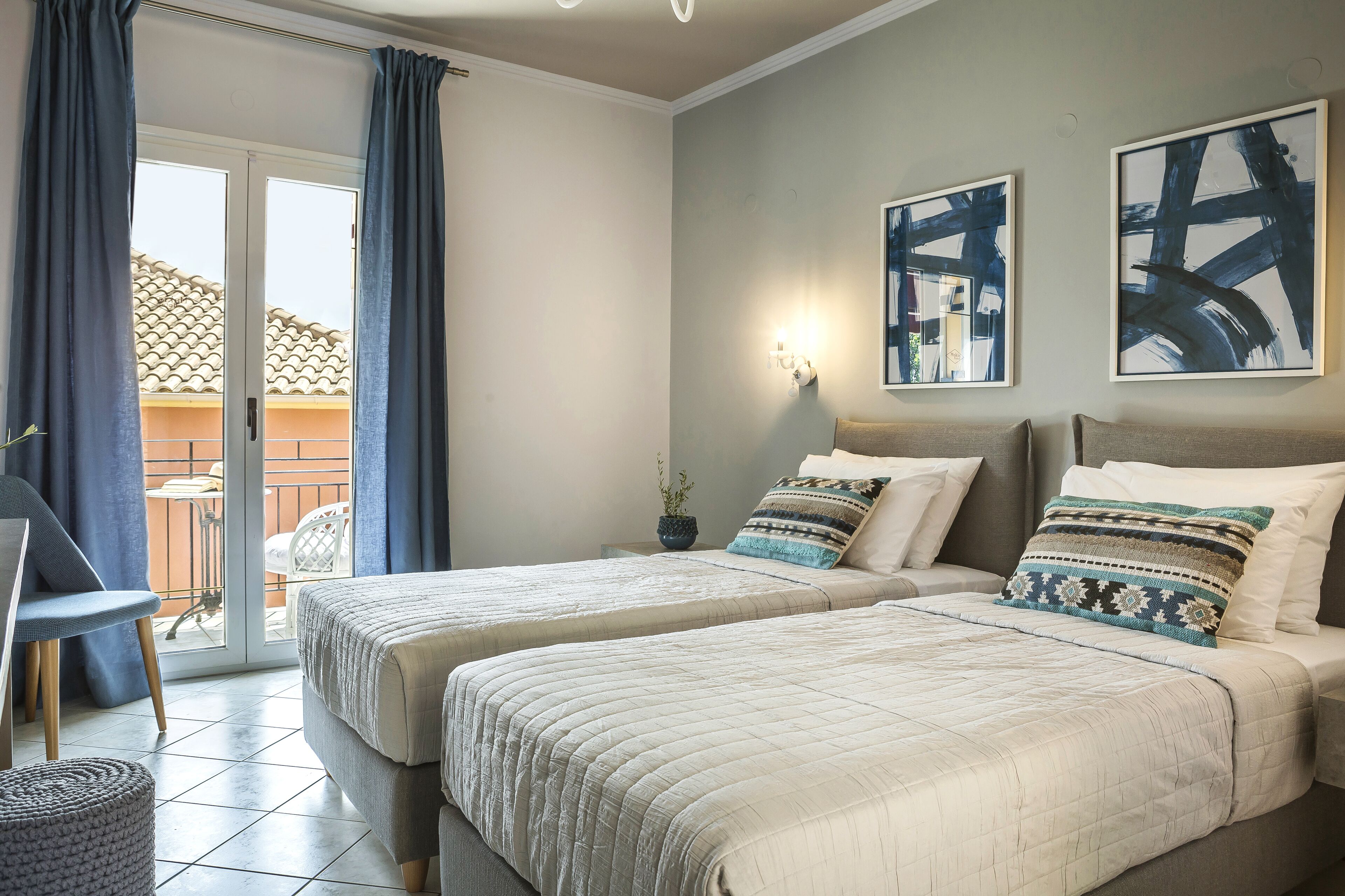 A hotel room with two beds, a chair, a small table, and a view of a balcony.