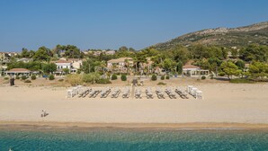 A beach resort with rows of sun loungers, a clear blue sea, and houses in the background. - Makis Hotel Skala (Kefalonia)
