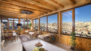 A dining area with wooden beams, large windows, and a view of a town.