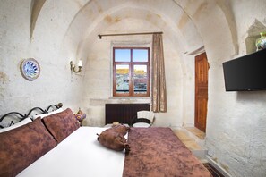 A narrow room with a bed, a chair, a window, and a television. - Romantic Cave Hotel (Ürgüp)