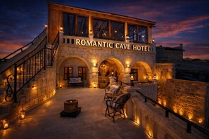 The exterior of the Romantic Cave Hotel with stone architecture, a staircase, outdoor seating area, and a fire pit. - Romantic Cave Hotel (Ürgüp)