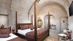 A bedroom with a four-poster bed, a wooden headboard, a bedside table with a lamp, and a small shelf with decorative items.