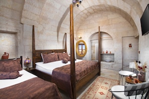 A bedroom with a four-poster bed, a wooden headboard, a bedside table with a lamp, and a small shelf with decorative items. - Romantic Cave Hotel (Ürgüp)
