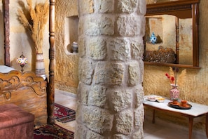 A room with a stone pillar, a wooden bed, a small table with a vase, and a mirror on the wall. - Romantic Cave Hotel (Ürgüp)