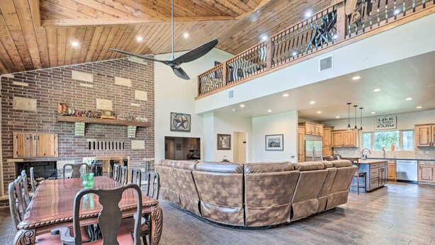 A spacious living area with a fireplace, a high ceiling with a fan, and a kitchen with wooden cabinets.