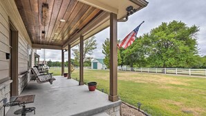 A covered porch with outdoor seating, a flag, and a view of a fenced property.