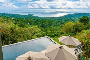 A pool with two umbrellas, surrounded by lush greenery and a view of the ocean. - Casa Amigos - Breathtaking Luxe Ocean View Villa (Bahía Ballena)