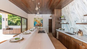 A modern kitchen with a marble countertop, wooden cabinets, and a long island with seating. - Resol Luxury Oceanview Villa in Costa Rica (Bahía Ballena)