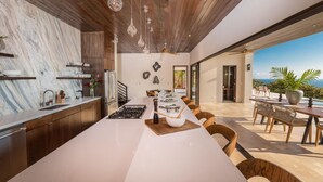 A modern kitchen with a large island, wooden ceiling, and a view of the ocean. - Resol Luxury Oceanview Villa in Costa Rica (Bahía Ballena)