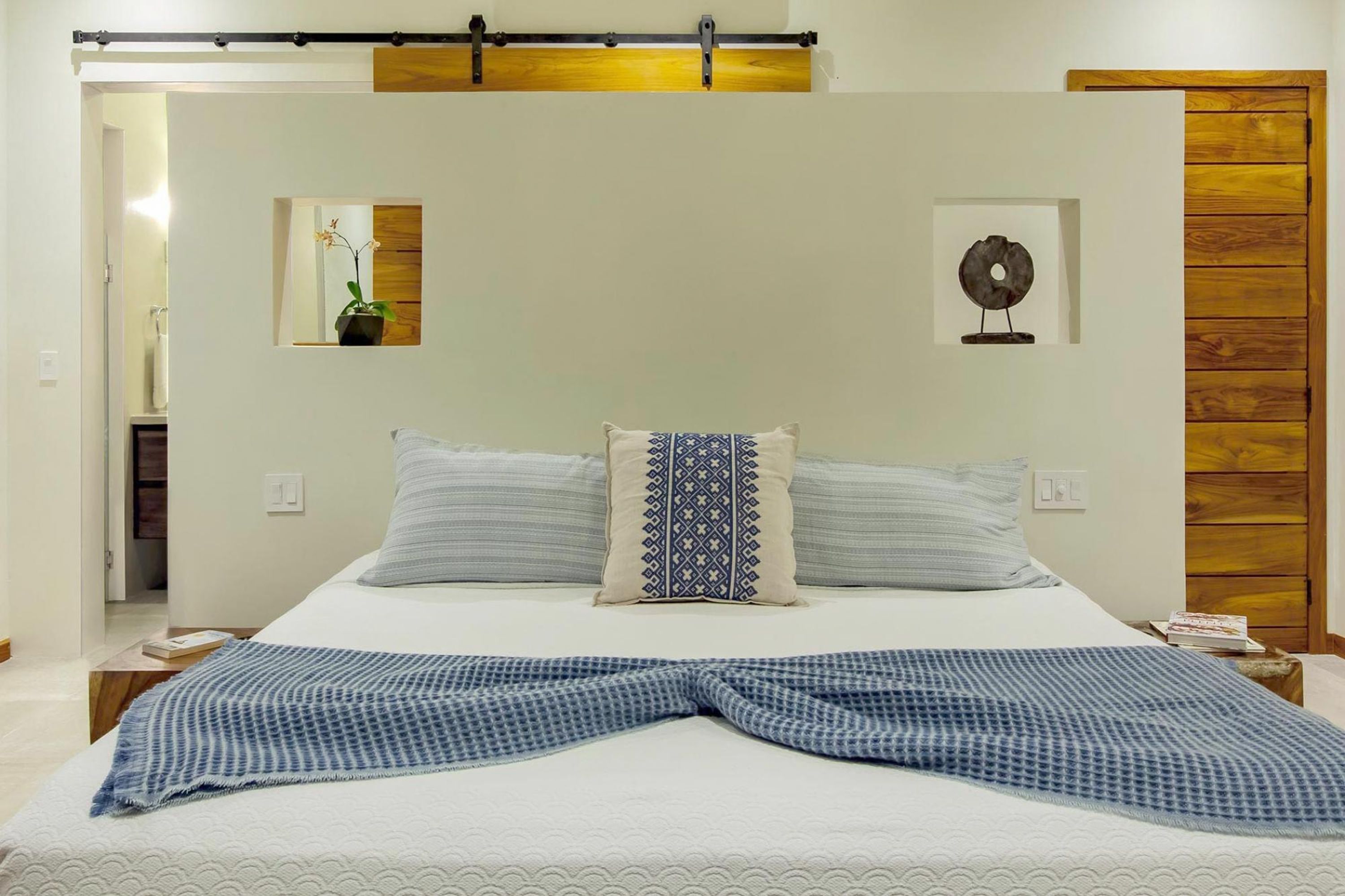 A bedroom with a large bed, two pillows, a blue blanket, a wooden headboard, and a small bedside table with a book.