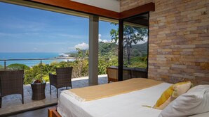 A bedroom with a large bed, a view of the ocean, wicker chairs, and a small table with fruit. - Luxe 4 Bdrm Villa w Epic Oceanview Infinity Pool (Bahía Ballena)