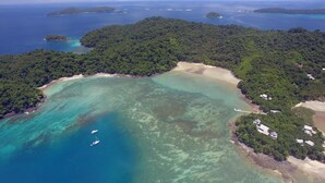 An aerial view of a tropical island with a clear turquoise lagoon, a sandy beach, and dense green forest. - Luxe 4 Bdrm Villa w Epic Oceanview Infinity Pool (Bahía Ballena)