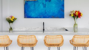 Une cuisine moderne avec un plan de travail en marbre blanc, un tableau abstrait bleu et des chaises en osier.