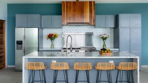 Une cuisine moderne avec des meubles gris, un îlot en marbre, des tabourets de bar en osier et un ventilateur de plafond.