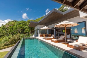 A modern house with a swimming pool, outdoor seating, and a view of the surrounding greenery.