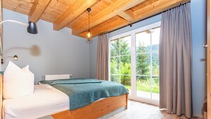 A bedroom with a wooden bed, a nightstand, a lamp, and a large window with curtains.