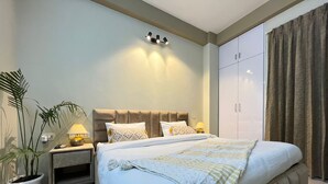 A modern bedroom with a large bed, bedside tables, a wardrobe, and a potted plant. - BedChambers Serviced Apartments Gurgaon (Gurugram)