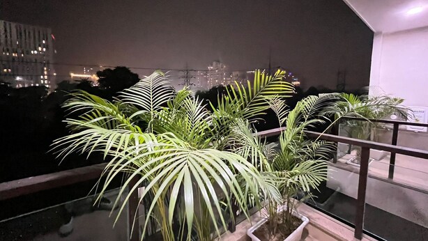 A balcony with potted plants, a railing, and a cityscape view at night. - BedChambers Serviced Apartments Gurgaon (Gurugram)