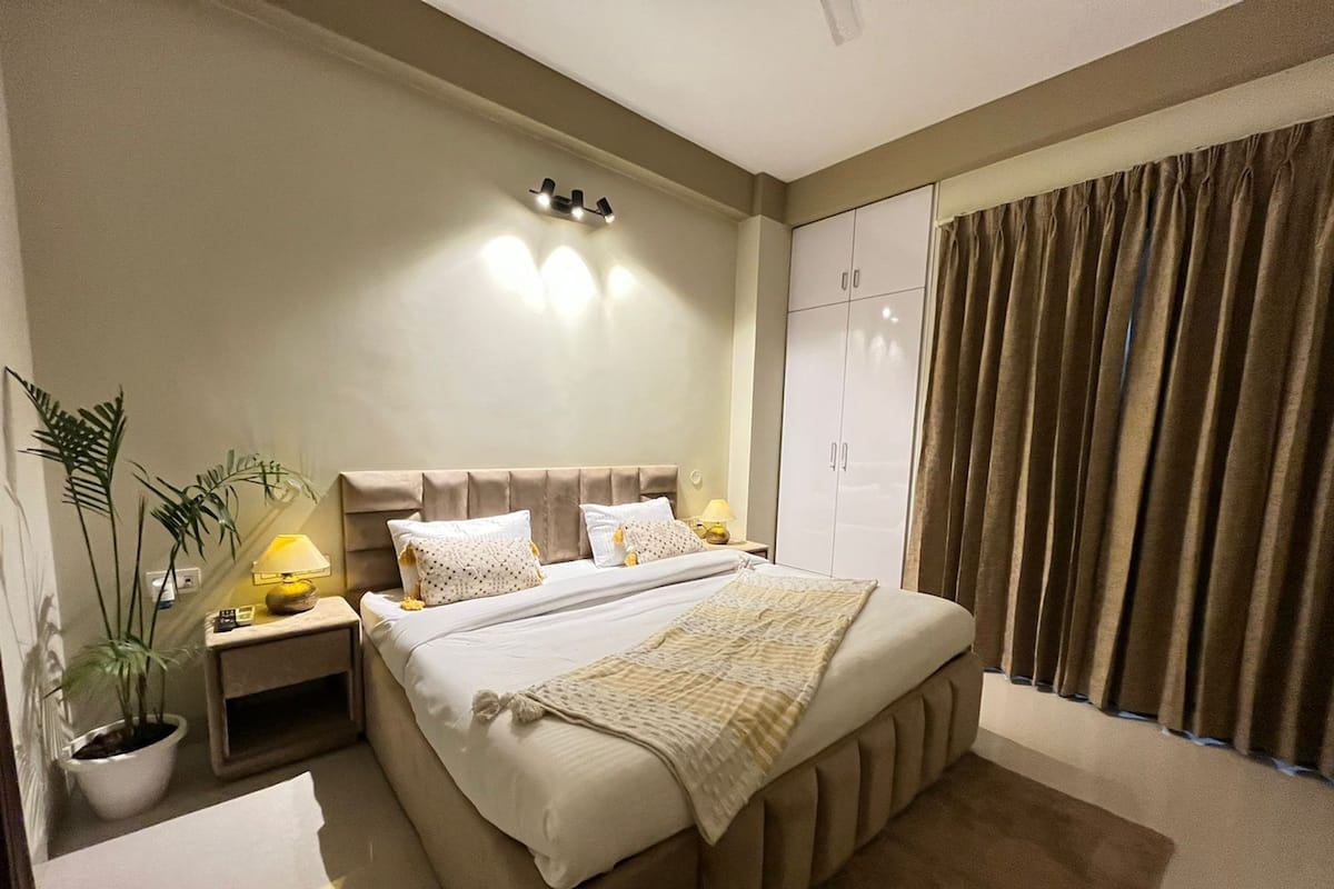 A modern bedroom with a large bed, bedside lamps, a potted plant, and a wardrobe.