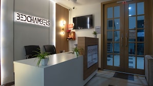 A reception desk with a sign reading "BEDCHAMBERS," a flat-screen TV mounted above, and a door with a biometric fingerprint scanner. - BedChambers Serviced Apartments Gurgaon (Gurugram)