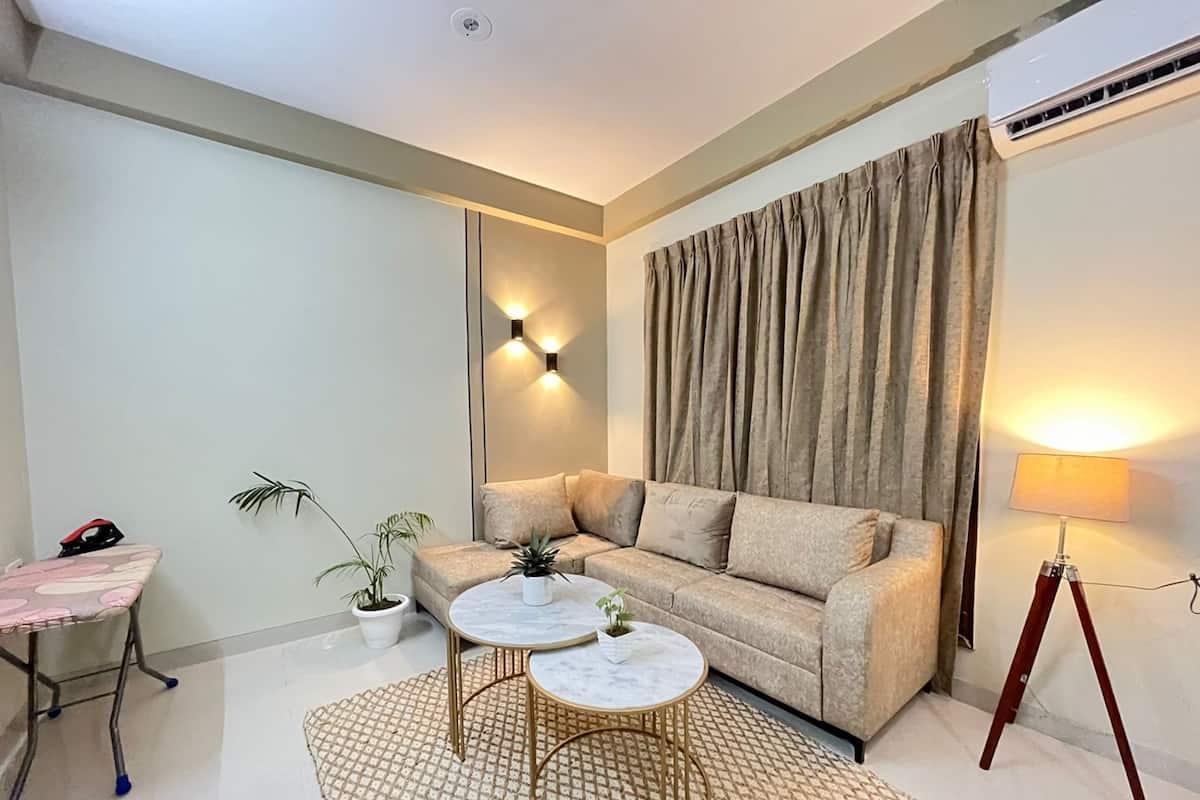 A modern living room with a sofa, two round tables, a small ironing board, and a lamp.