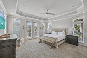 A bedroom with a large bed, a ceiling fan, and a view through the glass doors.