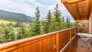 Ein hölzerner Balkon mit Blick auf eine gebirgige Landschaft und ein Dorf darunter.