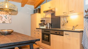 Eine moderne Küche mit Holzausstattung, einem Edelstahlbackofen, einer Spülmaschine und einer Hängelampe.