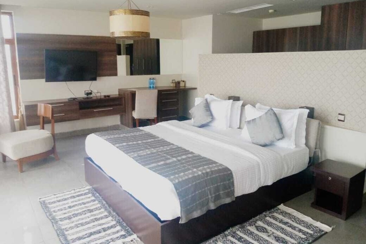 A modern bedroom with a large bed, a flat-screen TV mounted on the wall, a desk, and a chair.