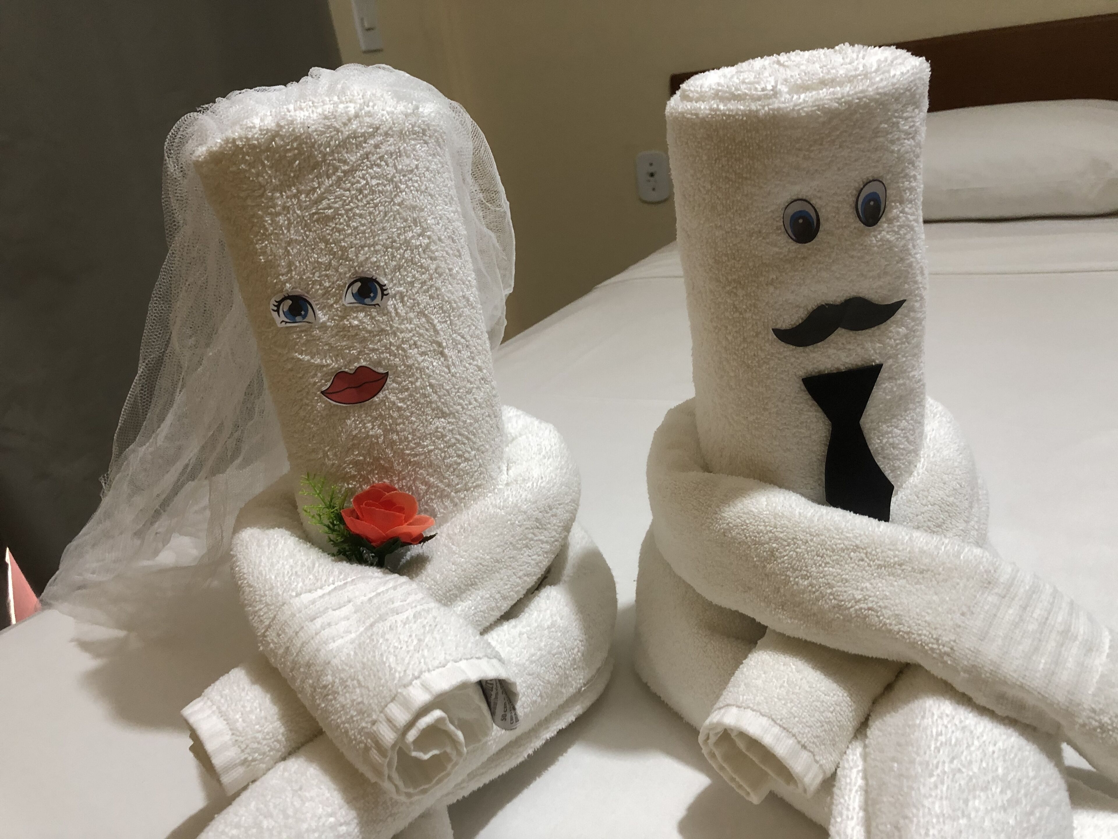 Dos toallas con adornos que parecen rostros, una con un velo de novia y la otra con bigote.