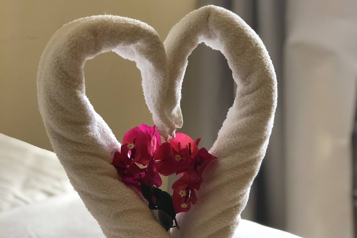 Un lit avec du linge de lit blanc et un cœur fait avec une serviette, décoré de fleurs.