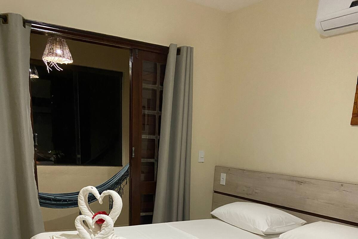 Une chambre d’hôtel avec un lit, une fenêtre avec des rideaux, un hamac et un climatiseur fixé au mur.
