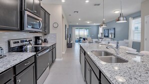 Una cocina moderna con armarios oscuros, electrodomésticos de acero inoxidable, encimeras de granito e iluminación colgante.