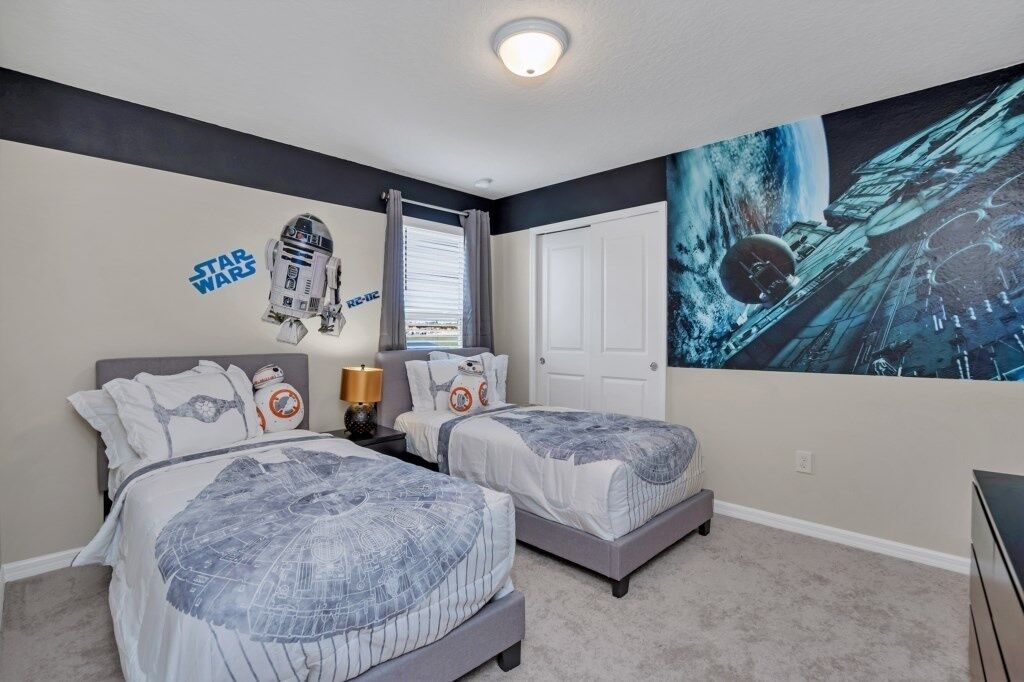 Een slaapkamer met twee bedden, Star Wars-decoratie, een groot muurschildering met een ruimte thema en een raam met gordijnen.